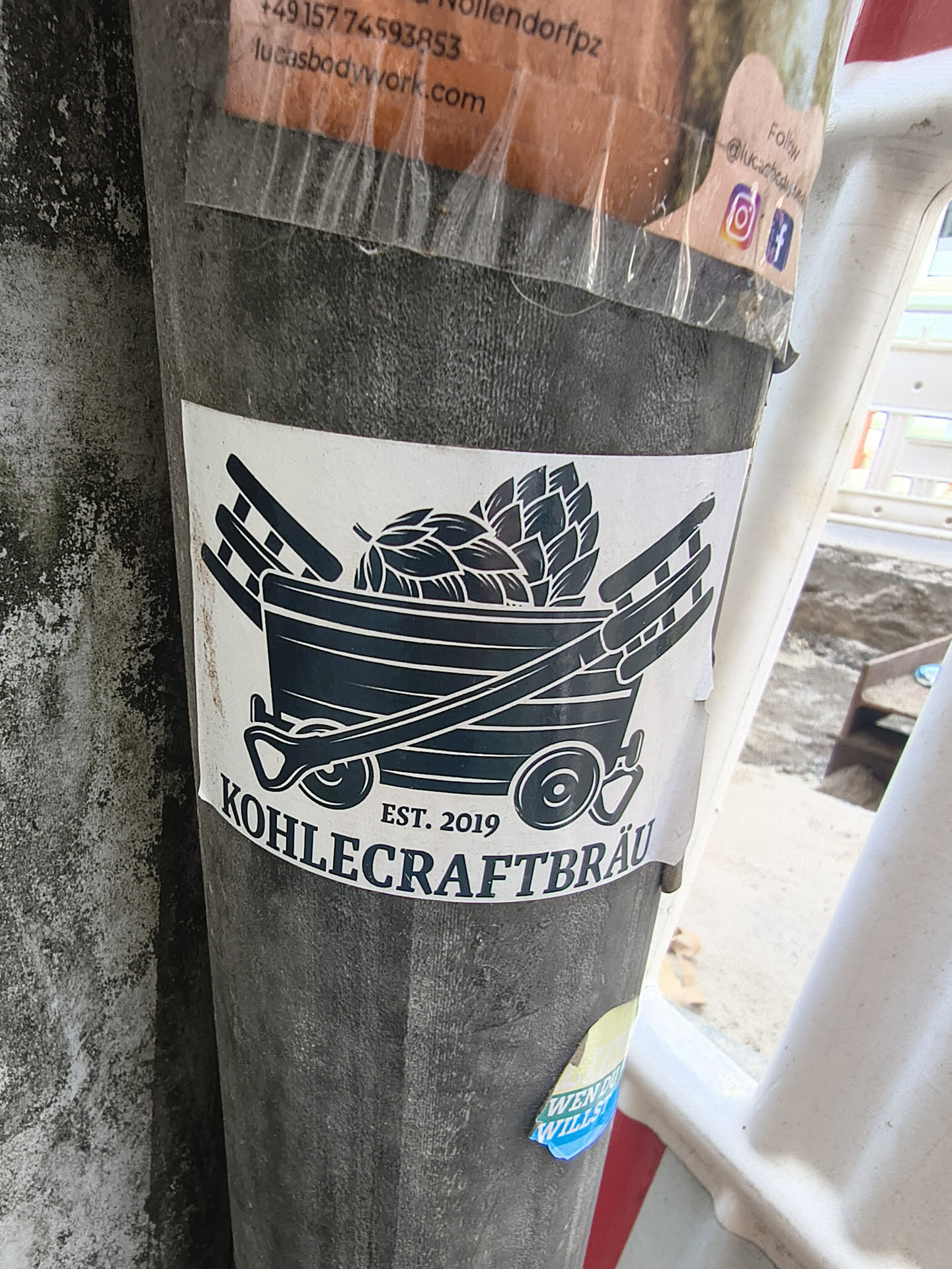 A white sticker depicting a dark blue mining cart loaded with hops. A shovel rests diagonally across the front, flanked by two ladders. The text 'EST. 2019' and 'KOHLECRAFTBRÄU' is printed below.