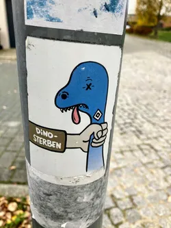 Street sticker The sticker features a cartoonish blue dinosaur head with an 'X' for an eye and a drooping, pink tongue, indicating distress or death. Its neck is clutched by a pale-skinned hand, as if being strangled. On the wrist of the hand, a brown banner or sign is depicted, containing German text. A small, black and white diamond-shaped logo, resembling the Hamburger SV (HSV) football club emblem, is visible on the dinosaur's neck. The entire illustration is outlined in black on a white rectangular background, adhered to a grey pole, showing signs of wear and slight peeling at the edges.