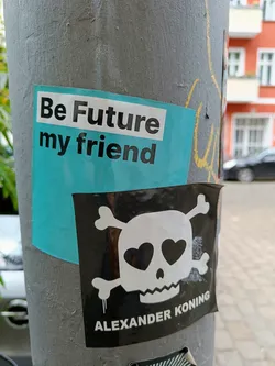 Street sticker A sticker featuring a skull with hearts for eyes and crossbones on a black background.  A teal sticker above it says "Be Future my friend". The sticker is signed "Alexander Koning"
