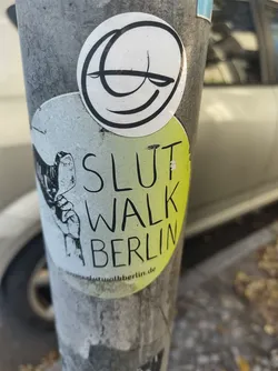 Street sticker A sticker featuring the text "SlutWalk Berlin" and a small illustration of a hand.  There's also a separate smaller round sticker with a simple line drawing of a face above it.