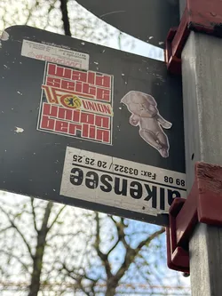 Street sticker The sticker depicts a light beige or off-white baby doll figure, rendered with subtle shading that gives it a three-dimensional, sculpted appearance. The baby is in a reclined or floating pose, with its head slightly tilted, eyes closed or downcast, and a somewhat pensive or grumpy expression. Its limbs are bent, characteristic of a classic doll posture. The overall aesthetic is reminiscent of a vintage porcelain or bisque doll, with a slightly eerie or melancholic feel. It is a die-cut sticker, precisely cut around the outline of the doll.