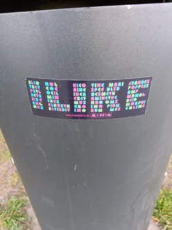 This sticker has a black background and pink and blue text. The text is organized in a vertical manner in columns and appears to be a list of names, possibly of people or brands. A website address is also included at the bottom of the sticker.