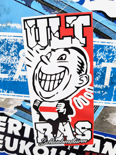 Street sticker A sticker featuring a cartoon face with a wide smile and the text "ULT RAS" in bold letters. The colors are predominantly black, red, and white.  There is smaller text at the bottom that reads "Schwabensturm".