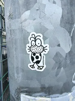 Street sticker The sticker features a whimsical, abstract cartoon creature rendered in stark black and white. Its large, round eyes with prominent black pupils gaze upwards, topped by two curled antennae. The snout area is filled with a dense pattern of black dots, from which thin whiskers extend horizontally. The creature's body is rounded and adorned with irregular solid black spots, reminiscent of polka dots. Two minimalist, geometric legs, ending in triangular feet, support the body. A clean white border outlines the entire figure against the grey, textured metal pole it is adhered to. The word 'weltformen' is printed vertically along the right side of its body.