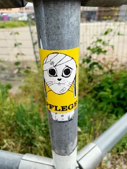 A yellow sticker featuring a cartoon bunny with a bandage on its head. The word 'PFLEGE' (care) is written below the bunny, along with a small cityscape graphic. The style is simple and slightly melancholic. The sticker is affixed to a metal pole outdoors.