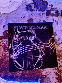 A sticker featuring abstract art with a person in the center. The background is dark and the main figure is outlined with bright pink lines. The text 'VOKALMATADOR' is written at the top of the sticker.