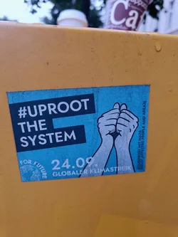 Street sticker A sticker advocating for climate action with the text '#Uproot The System', '24.09. Globaler Klimastreik', and 'For Future'. It features two hands clasped together, symbolizing unity and action.