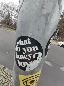 A round black and white sticker on a metal pole. The text on the sticker is in a retro style font.