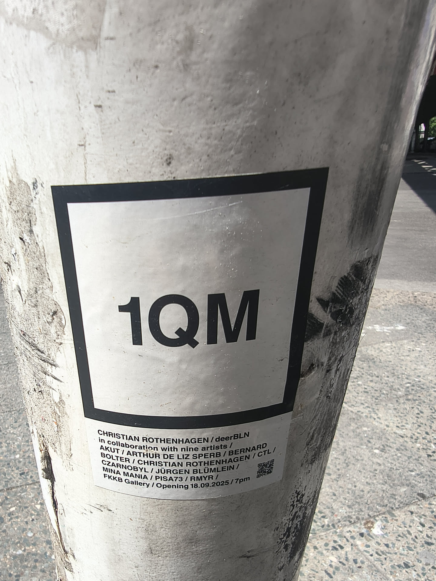 A white rectangular sticker affixed to a concrete pillar. It features the bold black text '1QM' inside a black square border. Below, smaller text lists participating artists, the venue 'FKKB Gallery', an opening date of '18.09.2025', and a small QR code in the corner.