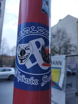 Street sticker This sticker shows the logo for Alphaönix Society. The logo is primarily blue and white, with a circular design incorporating a joker-like face, a stylized letter 'P', and a phoenix. The text "Alphaönix Society" is visible at the bottom. The overall style is bold and graphic.