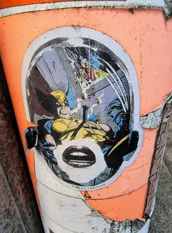 Street sticker The sticker shows Wolverine in a comic book style, with a pair of lips added over the face. The sticker is on a peach-colored object.