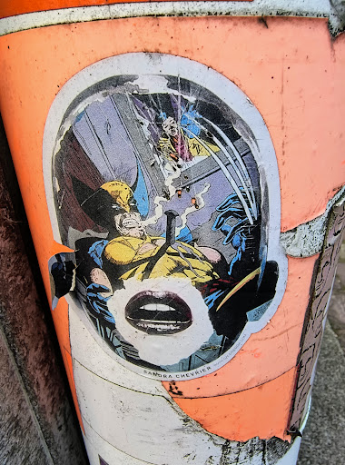 The sticker shows Wolverine in a comic book style, with a pair of lips added over the face. The sticker is on a peach-colored object.