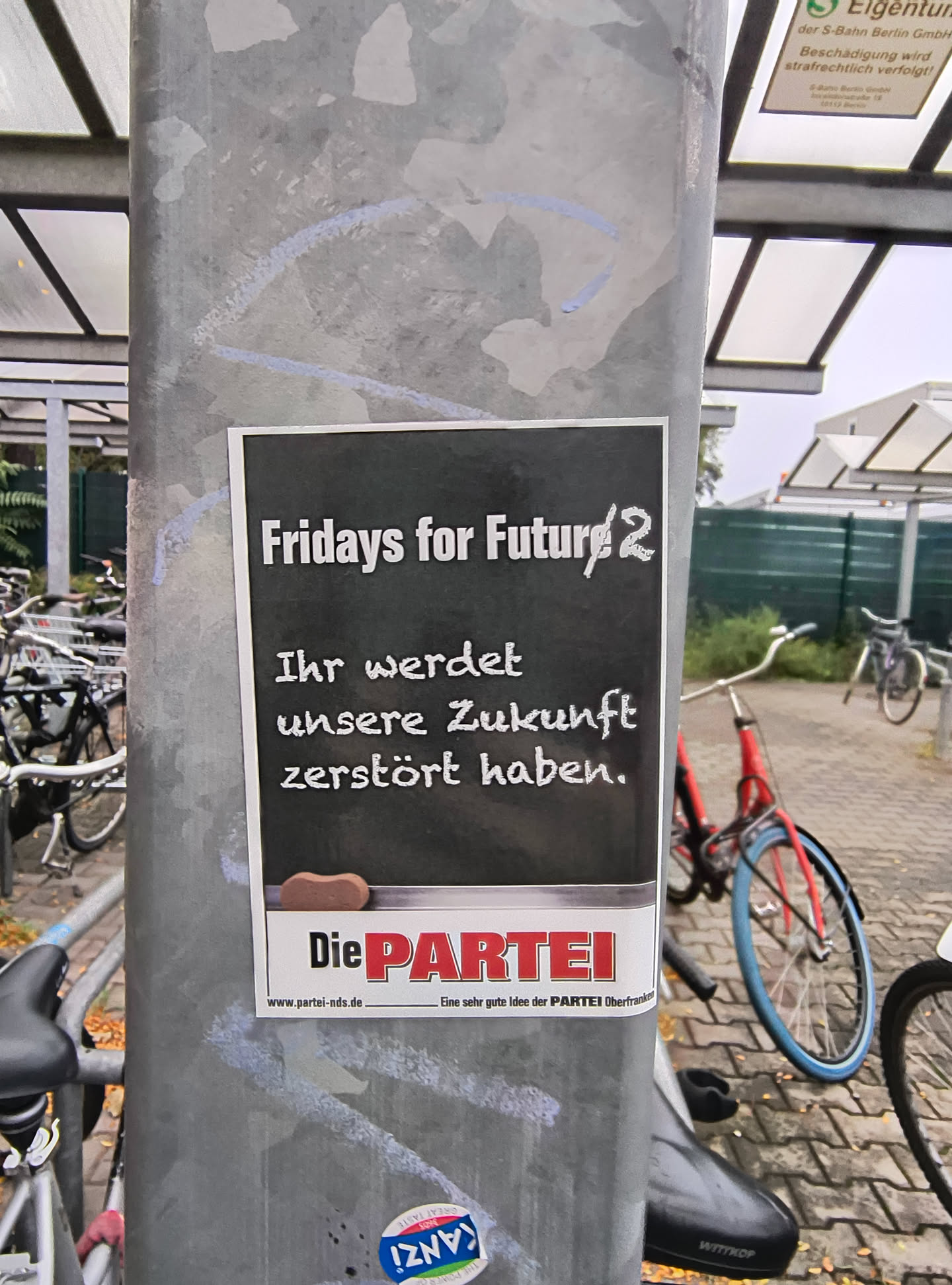 The sticker is predominantly black with white text. At the top, it reads 'Fridays for Future 2' in a stylized font. Below this, in a more handwritten-style font, it says 'Ihr werdet unsere Zukunft zerstört haben.' (You will have destroyed our future.). At the bottom, there is a white banner with the logo 'Die PARTEI' in red and white, and a website address 'www.partei-nds.de' followed by 'Eine sehr gute Idee der PARTEI Oberfranken'. A small, brown, bean-shaped object is placed just above the 'Die PARTEI' logo.