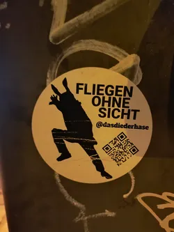 Street sticker A round sticker with a black silhouette of a person in a dynamic pose, seemingly jumping or falling. The text "FLIEGEN OHNE SICHT" is written above the figure, which translates to "Flying without sight" in German.  A QR code and Instagram handle are included at the bottom.