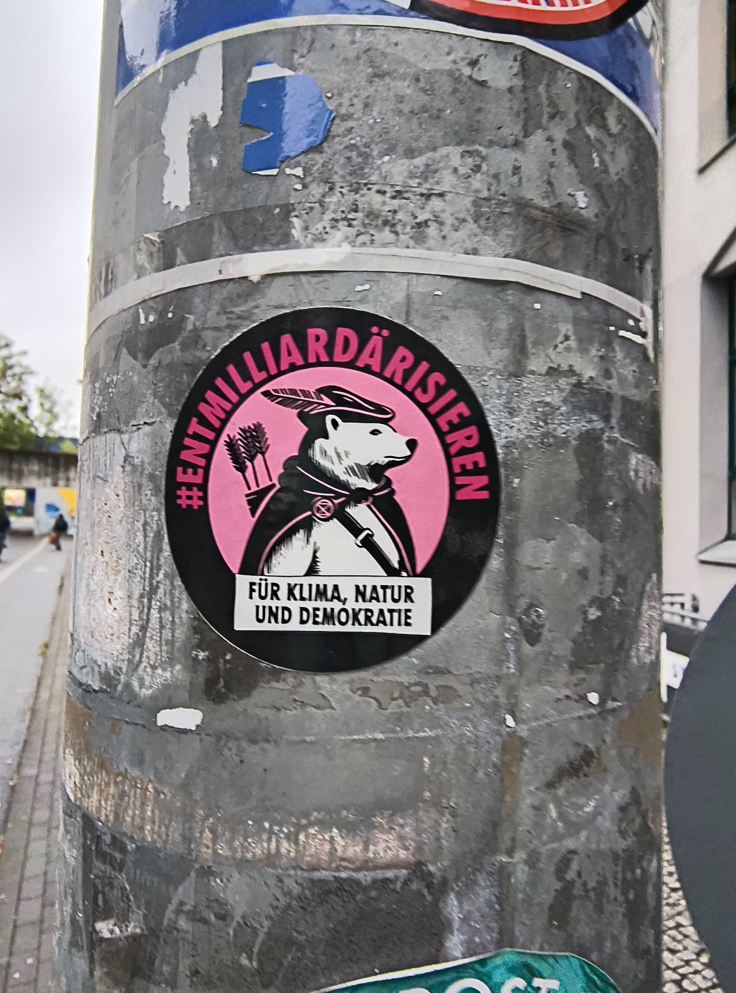 The sticker is circular with a black border. The background inside the circle is bright pink. In the center, there is an illustration of a polar bear wearing a hat with a feather and a cape. The polar bear is holding a quiver of arrows. Below the illustration, there is a white rectangular banner with black text. The overall design is bold and graphic.