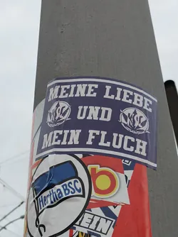 Street sticker A sticker with German text that translates to "My love and my curse." It features two logos, possibly of sports teams or organizations, flanking the text. The color scheme is mainly purple and white.
