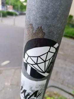 Black and white sticker of a diamond with the text "Moonyu Market" on it. The sticker is on a grey pole.