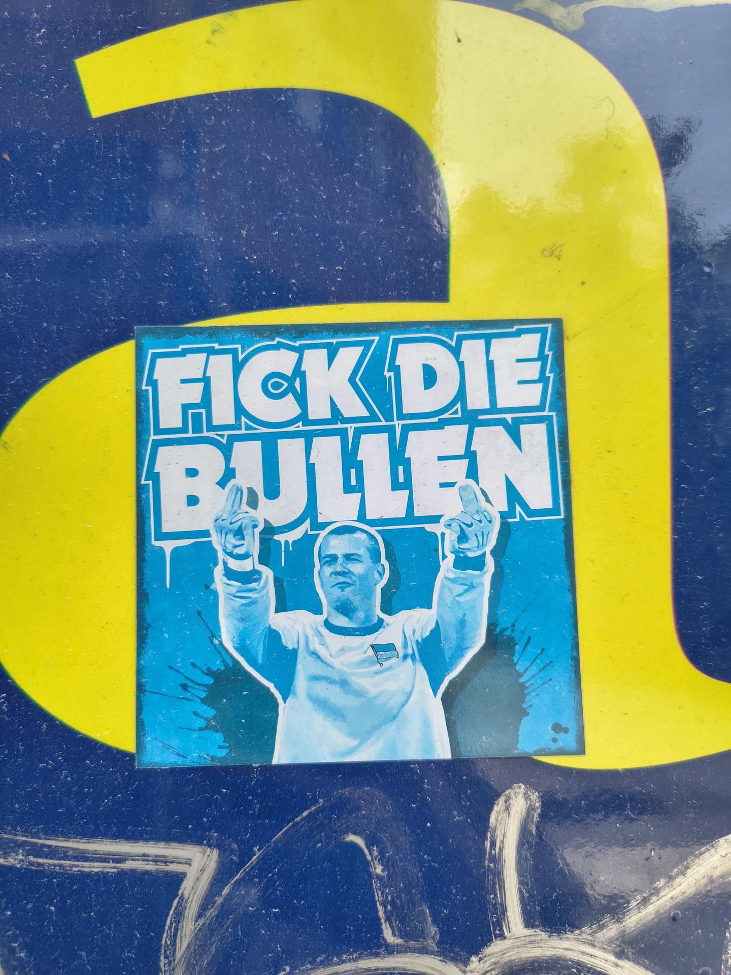 Square blue sticker depicting a Hertha BSC supporter raising both middle fingers. Bold white German text 'FICK DIE BULLEN' is displayed at the top against a blue, paint-splattered background.