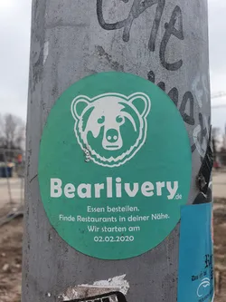 Street sticker A teal circular sticker featuring a white bear illustration and the text "Bearlivery.de". Below the logo, it reads: "Essen bestellen. Finde Restaurants in deiner Nähe. Wir starten am 02.02.2020."  which translates to: "Order food. Find restaurants near you. We start on 02.02.2020."