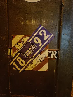 A sticker featuring the Hertha BSC logo and the year 1892. The sticker is purple and gold and is adhered to a dark-colored surface.