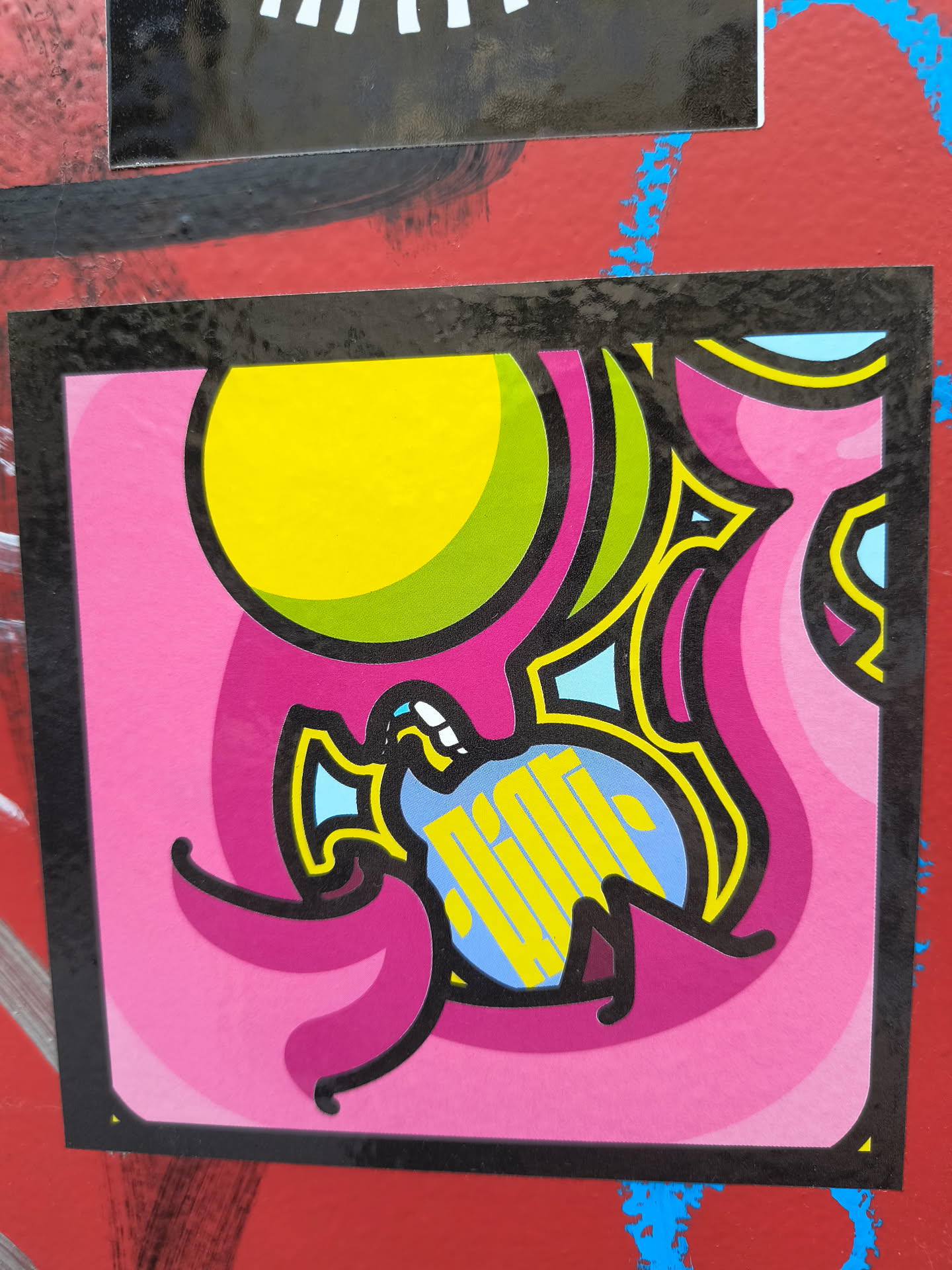 A square sticker with a black border features a whimsical, abstract design in vibrant colors. A yellow and green circle sits at the top left. An abstract creature is depicted in the center with bright yellow stripes over a blue body. The background is filled with pink and magenta swirls, adding to the playful and surreal atmosphere.