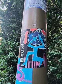 Street sticker This vibrant sticker features a figure with a blue body and a dark cloud-like head adorned with lightning bolts. The background is black with pink accents, and there is an Instagram handle "@HERE.MW" visible on the left side. Another sticker below it is visible with an "S" shape in pink.