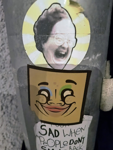 A sticker featuring a cartoonish happy face and a separate sticker of a laughing person. A handwritten note below says: "Sad when people don't smile back"