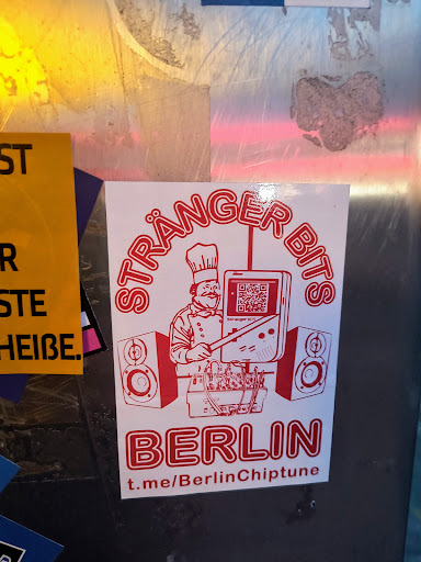 Street sticker A white square sticker with red ink. It features a chef using a modified Gameboy to play chiptune music, positioned between two speakers. Text includes "STRÄÄNGER BITS" around the top, "BERLIN" at the bottom, and a Telegram link. The QR code on the gameboy screen leads to a URL related to chiptune music or the artist.