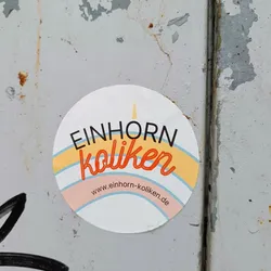 Round sticker with the text "EINHORN koliken" in black and orange. It has a rainbow-like arc underneath. The website www.einhorn-koliken.de is printed at the bottom.