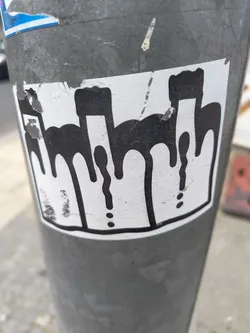 Street sticker A sticker with a black outline and dripping shapes. The shapes are arranged horizontally and the dripping effect is pronounced. The background is white and the sticker appears to be affixed to a metal pole.