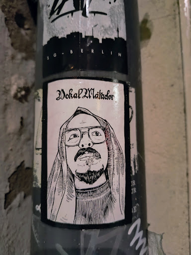 Street sticker The sticker shows a black and white illustration of Vokal Matador, a person with glasses and a head covering, smoking a cigarette. The text 'Vokal Matador' is written in gothic font above the portrait.