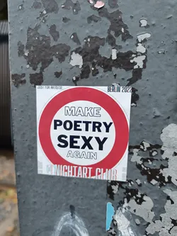 Street sticker Round sticker with the text "Make Poetry Sexy Again" in the center.  It has a red circle border with white text. At the bottom it says @NightArtClub.  There is additional small text at the top that says "Just for Artists" and "Berlin 2022". The sticker is affixed to a weathered gray surface.