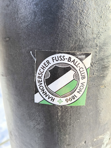 Street sticker A sticker with the Hannover 96 football club logo is affixed to a dark gray metal post. The logo features the club name encircling a shield with black and green stripes, along with the founding year of 1896.