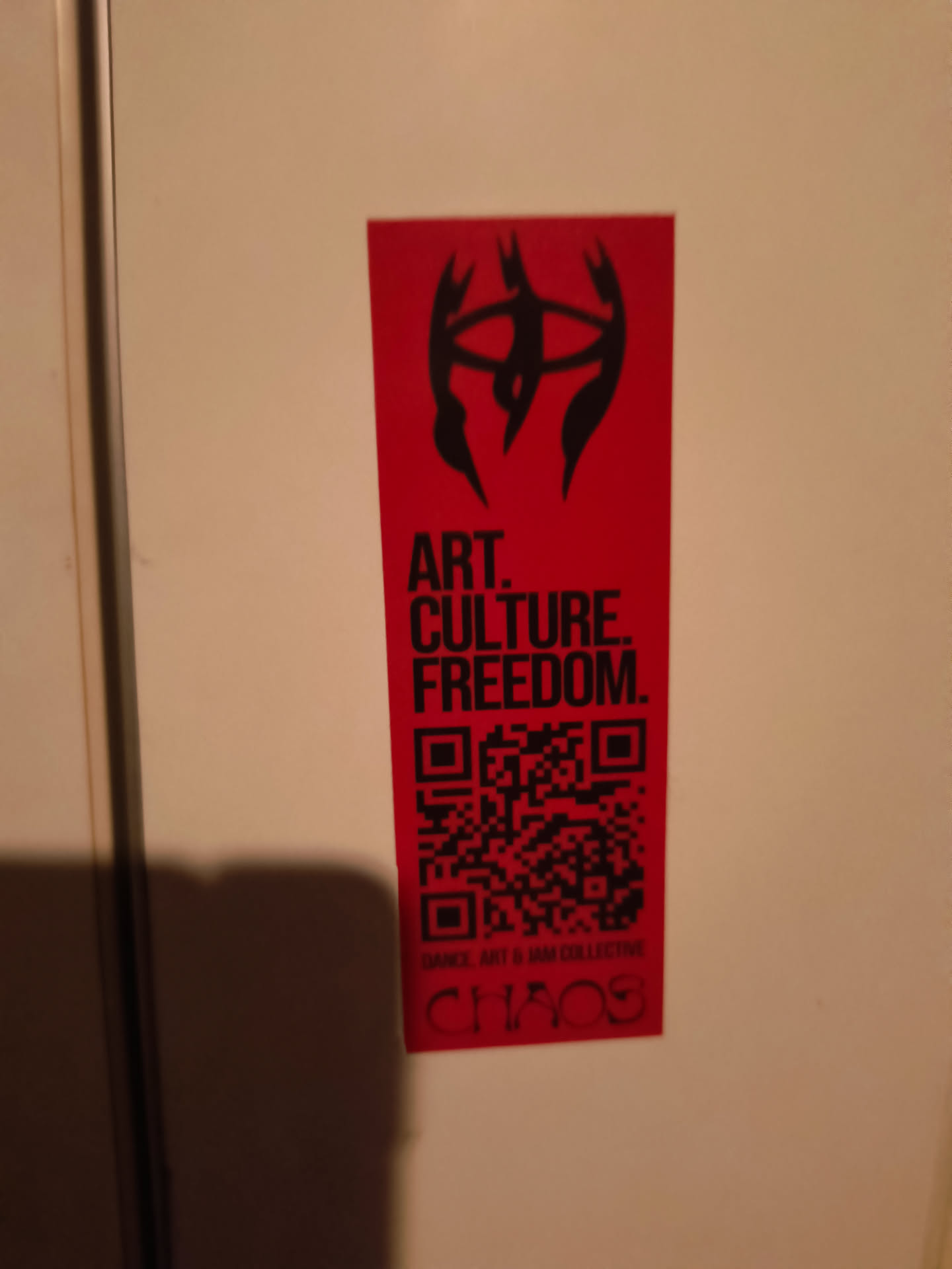 The sticker is predominantly red with black graphics and text. At the top, there's a stylized black symbol resembling an abstract face or creature with sharp, angular features and what appear to be multiple eyes. Below this symbol, the words 'ART. CULTURE. FREEDOM.' are printed in bold, uppercase black letters. Beneath the text is a QR code, also in black. Finally, at the bottom, smaller black text reads 'DANCE, ART & IAM COLLECTIVE' above the word 'CHAOS' in a distressed, stylized font.