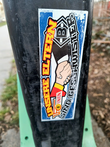 Street sticker A sticker featuring a handshake, symbolizing the Union Berlin and Borussia Mönchengladbach football clubs' fans. On the left side, there's a hand in the Union Berlin team colors (red and yellow), and on the right, a hand with the logo of Borussia Mönchengladbach. The text reads "UNSERE ELTERN SIND GESCHWISTER" (our parents are siblings).