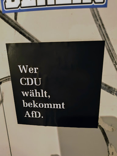 A political sticker with a black background and white text that says "Wer CDU wählt, bekommt AfD." It translates to "Whoever votes for CDU, gets AfD."