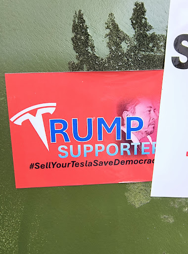 A red sticker with "TRUMP SUPPORTER" in blue text, using the Tesla logo as the "T" in "TRUMP". The sticker also features a portrait of Elon Musk and the hashtag "#SellYourTeslaSaveDemocracy".