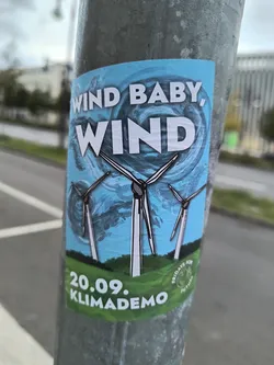 Street sticker The sticker features a vibrant blue sky with swirling clouds, evoking a sense of wind. In the foreground, three stylized wind turbines are depicted with white blades and dark outlines, set against a green, hilly landscape. The text 'WIND BABY, WIND' is prominently displayed in large, white, bold lettering across the top half of the sticker. Below the turbines, the date '20.09.' and the word 'KLIMADEMO' are written in white on a green band. To the right, a circular emblem with the text 'FRIDAYS FOR FUTURE' is visible.