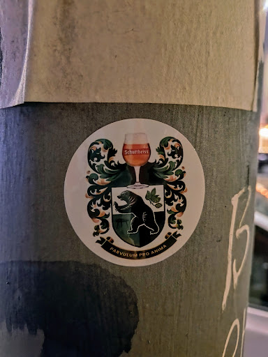 Round sticker with a coat of arms featuring a bear, hops, and a glass of Schultheiss beer. The motto 'Parvulvm Pro Anima' is written below the emblem.