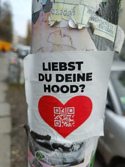 A sticker featuring a red heart with a QR code in the center.  The text on the sticker asks in German, "Do you love your Hood?"