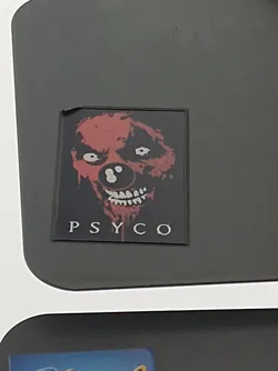 Street sticker A sticker featuring a scary clown face with the word "PSYCO" written underneath. The clown is depicted in red and black, with a bloody grin and large, white eyes.