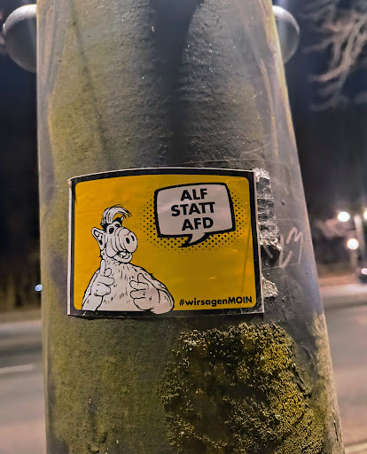 Street sticker A sticker featuring Alf from the TV show Alf, with a speech bubble saying "ALF STATT AFD".  The hashtag #wir sagenMOIN is also included.  The sticker is yellow with black text and image.