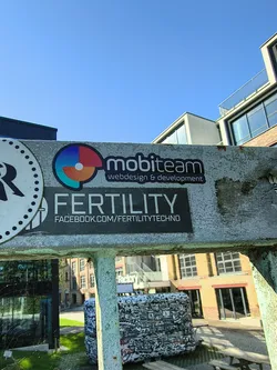 Street sticker A rectangular black sticker featuring the word 'FERTILITY' in large white sans-serif font, with the URL 'FACEBOOK.COM/FERTILITYTECHNO' printed below it. It is stuck to a weathered concrete beam.