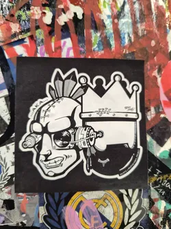 Street sticker The sticker is predominantly black and white with a thick white border. It depicts a stylized skull with a stitched forehead and feather headdress. The skull is equipped with intricate mechanical augmentations around the eye and jawline, suggesting a cyberpunk or futuristic theme. To the right of the skull, a crown is prominently featured, also in white. Subtle text appears on the crown and along the bottom curve of the sticker.
