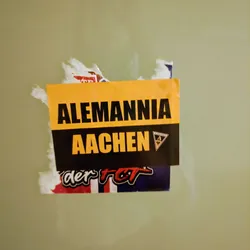 Street sticker A yellow and black sticker with the text "Alemannia Aachen" on it.  There is a smaller logo visible to the right of the text.  Part of another sticker is visible underneath.