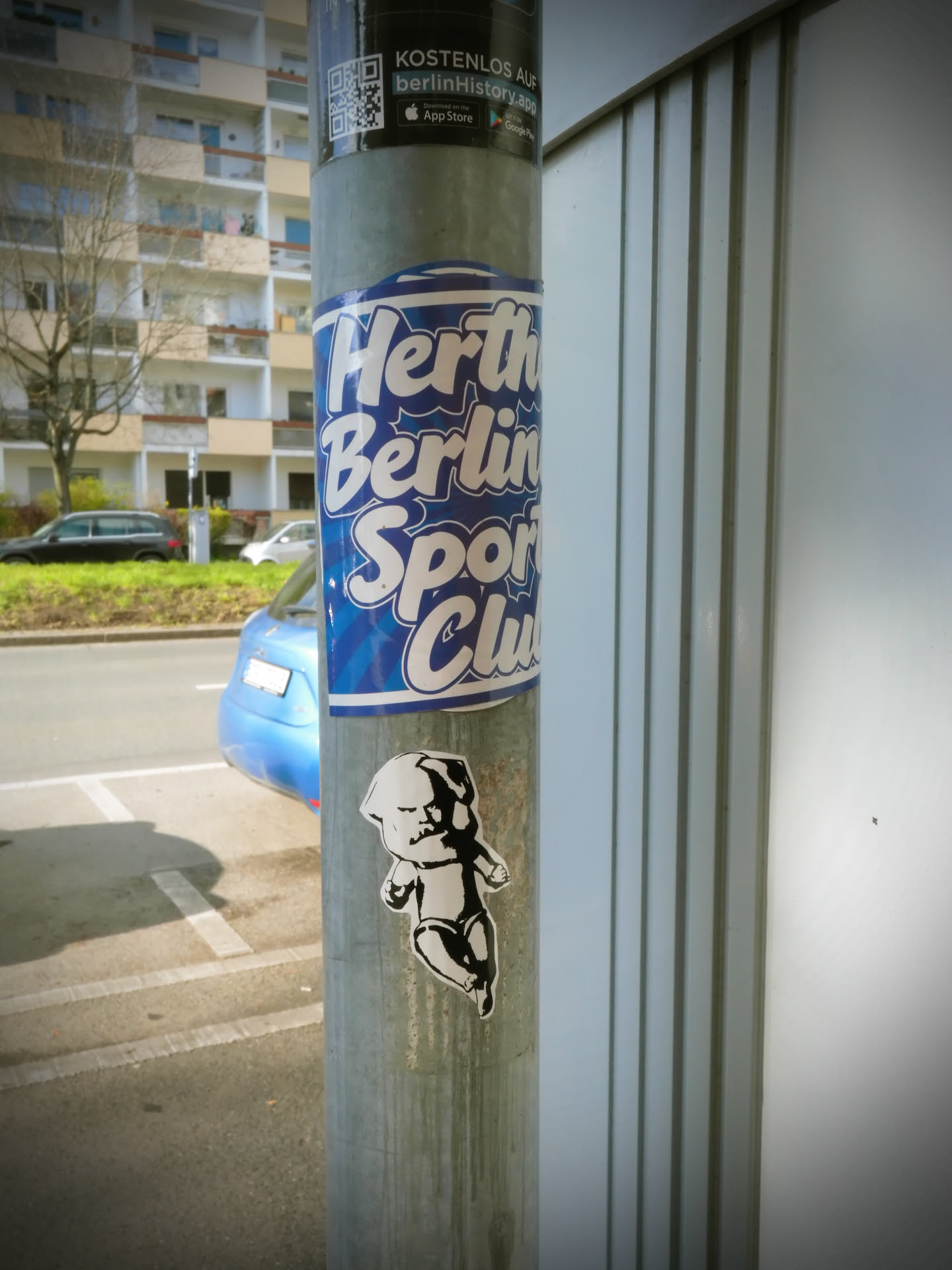 A vertically oriented, oval-shaped sticker featuring the text 'Hertha Berlin Sport Club' in bold, bubbly white letters with a thin white outline. The background is a vibrant blue with a subtle radial or sunburst pattern emanating from the center. The sticker is adhered to a metal pole, showing slight curvature and minor wear, indicating it is a genuine physical sticker.