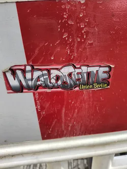Street sticker A sticker featuring the words "Waldseite Union Berlin" in a stylized graffiti font. The sticker is applied to a red surface, possibly a barrier or fence.