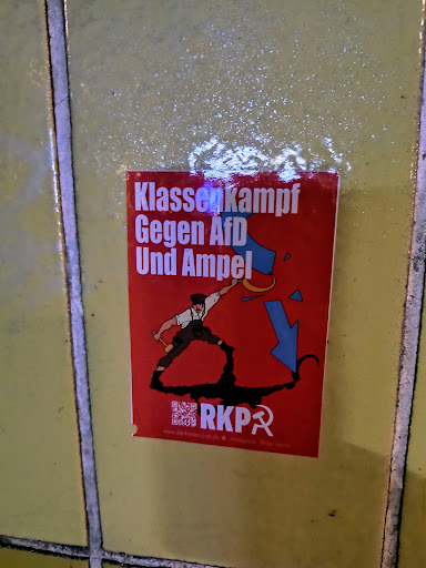 A red sticker with a cartoon illustration of a worker smashing a symbol, likely representing the AfD and Ampel coalition.  It includes text in German, a QR code, and the abbreviation RKPA. The sticker promotes class struggle against the AfD and Ampel coalition.