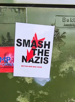 Street sticker The sticker is white with black text that reads "SMASH THE NAZIS". There is a red star graphic integrated into the word "SMASH". Underneath, in smaller text, it says "BETTER RUN NAZI SCUM".