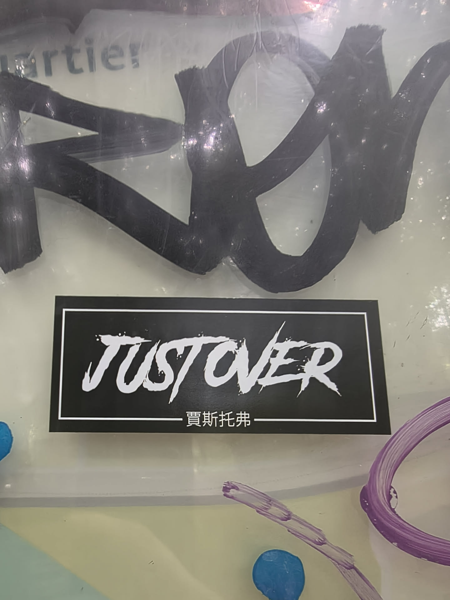 Rectangular black sticker with a white border. Features the stylized, distressed white text 'JUST OVER' and Chinese characters '賈斯托弗' at the bottom.